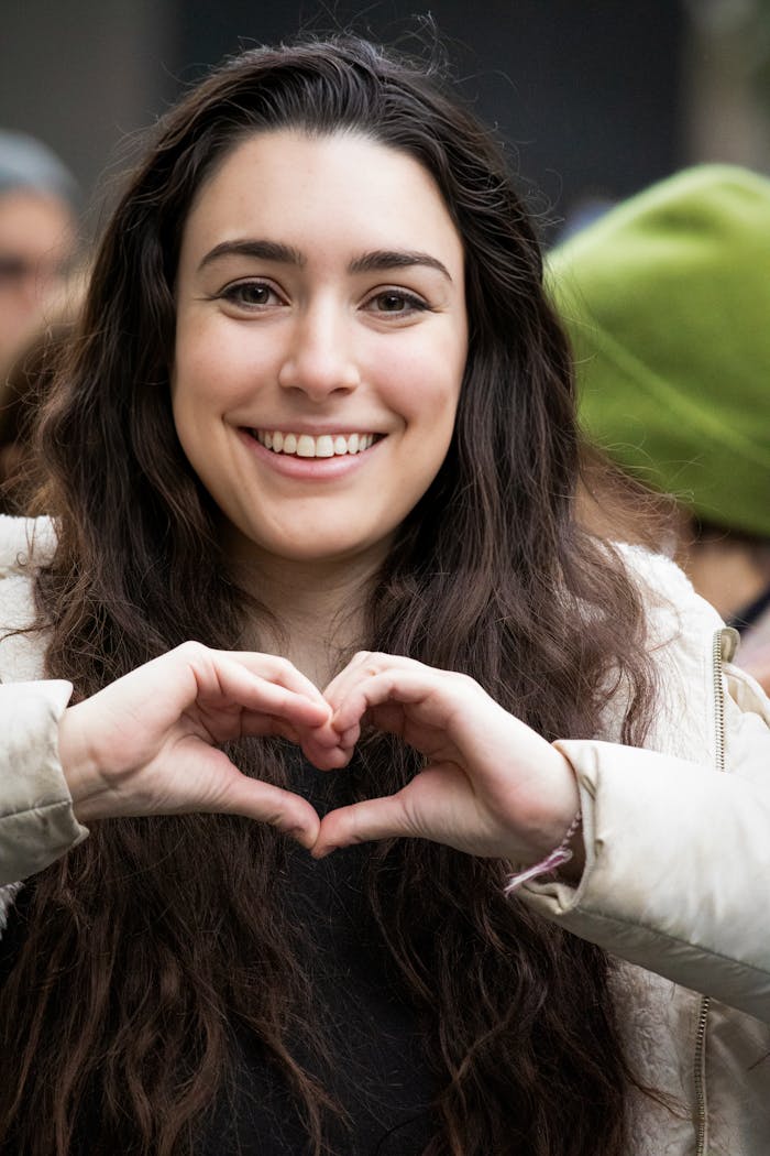 A happy woman in a urban setting making a heart shape with her hands, symbolizing love and positivity.