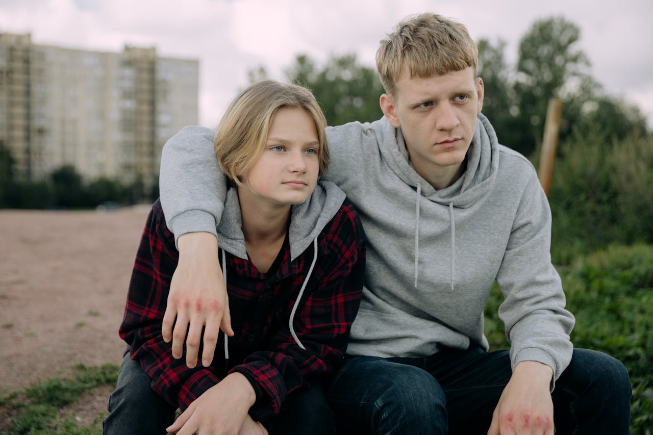 about-02 Two siblings in casual hoodies sit together outdoors, conveying a relaxed and thoughtful moment.