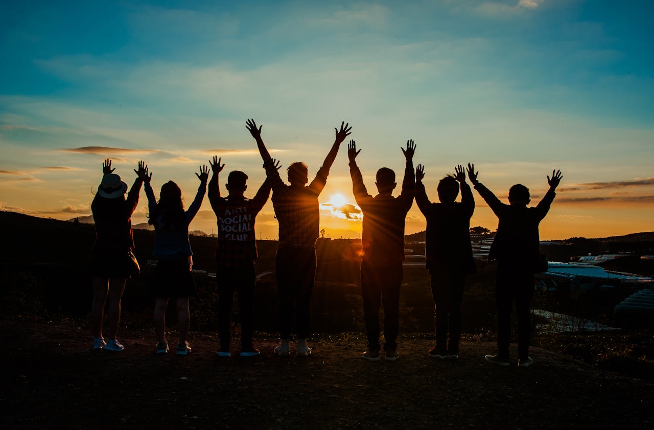 why-choose-us A diverse group of friends raises their arms in celebration against a vibrant sunset backdrop.